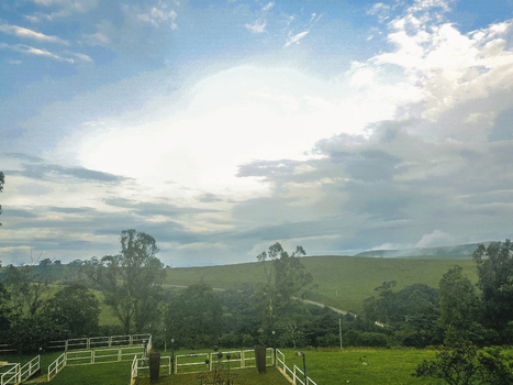 Aerial view of rolling green hills under a dramatic bright cloudy sky with white fences and tall trees framing the verdant landscape Obudu Cross River Nigeria.