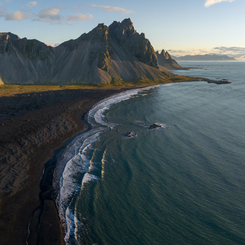 Aerial view of black sands meeting the turquoise sea beneath the jagged peaks of Vestrahorn mountain creating a stark contrast of textures Höfn Iceland. Aerial view of black sands meeting the turquoise sea beneath the jagged peaks of Vestrahorn mountain creating a stark contrast of textures Höfn Iceland.