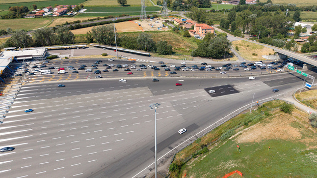 Aerial view of the Autostrada A1 toll plaza featuring multiple vehicle access lanes highway infrastructure and surrounding green landscape in Melegnano Lombardy Italy.