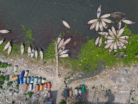 Aerial view of traditional wooden boats moored in circular patterns on the Buriganga River with colorful barrels and green vegetation in Dhaka Dhaka Division Bangladesh.