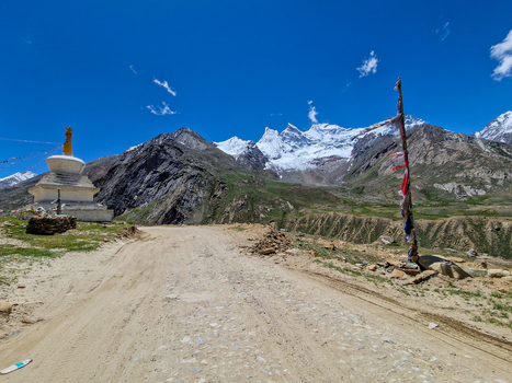 View of Penzi La road with a white Buddhist stupa colorful prayer flags and snow capped Himalayan peaks under a clear blue sky in Zanskar Ladakh India.