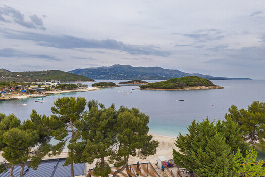 Aerial view of the turquoise waters and small islands of Ksamil with lush pine trees and a sandy beach under a cloudy sky in Ksamil Vlore County Albania. Aerial view of the turquoise waters and small islands of Ksamil with lush pine trees and a sandy beach under a cloudy sky in Ksamil Vlore County Albania.
