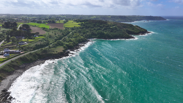 Aerial view of the rugged coastline of Locquirec featuring turquoise waves crashing against rocky cliffs and lush green fields under a bright sky in Locquirec Brittany France. Aerial view of the rugged coastline of Locquirec featuring turquoise waves crashing against rocky cliffs and lush green fields under a bright sky in Locquirec Brittany France.