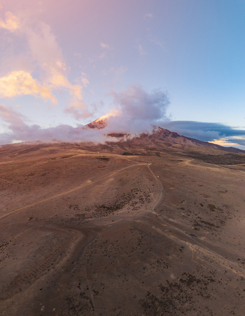 Aerial view of Volcano Chimborazo with its snow capped peak partially obscured by clouds rising above the arid rugged volcanic landscape under a soft sunset sky in Guano Chimborazo Ecuador. Aerial view of Volcano Chimborazo with its snow capped peak partially obscured by clouds rising above the arid rugged volcanic landscape under a soft sunset sky in Guano Chimborazo Ecuador.