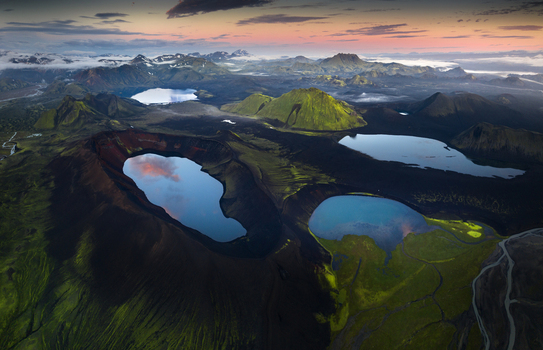 Aerial view of volcanic crater lakes surrounded by mossy green mountains and dark lava fields under a sunset sky Iceland.