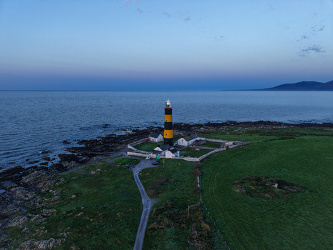 Aerial view of St. John s Point Lighthouse with its black and yellow stripes situated on the rocky coastline surrounded by green fields in Newcastle Northern Ireland United Kingdom. Aerial view of St. John s Point Lighthouse with its black and yellow stripes situated on the rocky coastline surrounded by green fields in Newcastle Northern Ireland United Kingdom.