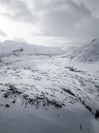 Aerial view of snow covered mountains and a winding road through a frozen valley under an overcast winter sky Ersfjord Troms Norway. Aerial view of snow covered mountains and a winding road through a frozen valley under an overcast winter sky Ersfjord Troms Norway.