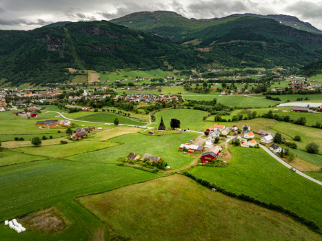 Aerial view of Hopperstad Stave Church surrounded by lush green fields traditional red farmhouses and rolling mountains under a cloudy sky in Vik i Sogn Vestland Norway. Aerial view of Hopperstad Stave Church surrounded by lush green fields traditional red farmhouses and rolling mountains under a cloudy sky in Vik i Sogn Vestland Norway.