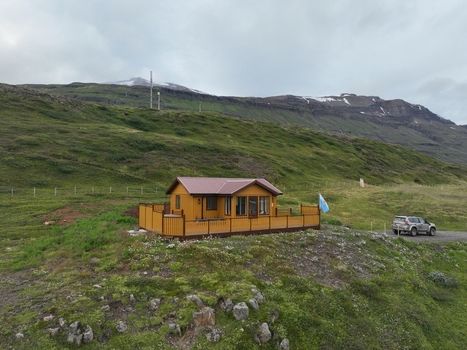 Aerial view of a wooden house nestled in the green hills with a car parked nearby under a cloudy sky in Seydisfjordur Mulathing Iceland.