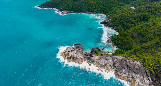 Aerial view of the coastline near Anse Soleil Beachcomber Hotel featuring large granite boulders turquoise water and lush tropical vegetation in Mahe Baie Lazare Seychelles.