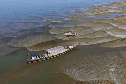 Aerial view of a traditional wooden boat with a thatched roof moored in a shallow river channel near a horse drawn cart on the mudflats in Joypurhat Rajshahi Division Bangladesh. Aerial view of a traditional wooden boat with a thatched roof moored in a shallow river channel near a horse drawn cart on the mudflats in Joypurhat Rajshahi Division Bangladesh.