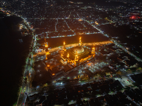Aerial view of the illuminated Baitul Muttaqien Mosque at the East Kalimantan Islamic Center surrounded by the glowing city lights of Samarinda East Kalimantan Indonesia.