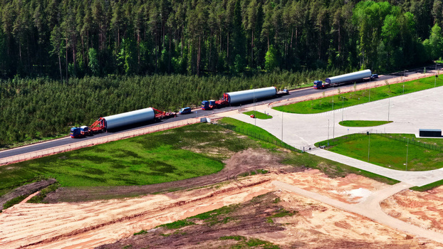 Aerial view of trucks transporting large wind turbine blades along a road bordering a forest in Latvija. Aerial view of trucks transporting large wind turbine blades along a road bordering a forest in Latvija.