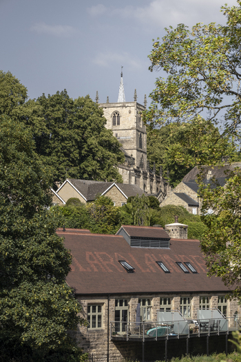 View of the historic St John the Baptist Church rising above stone buildings and lush green trees in Knaresborough England United Kingdom.