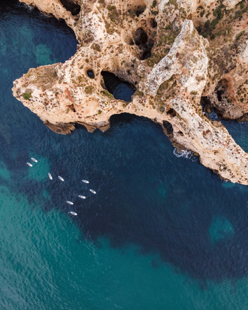 Aerial view of people doing kayak along the coastline near the caves in Ponta da Piedade with scenic cliffs in summertime Lagos Algarve region Portugal.
