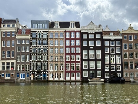 View of traditional narrow canal houses with ornate gables and large windows reflecting on the water in Amsterdam Netherlands. View of traditional narrow canal houses with ornate gables and large windows reflecting on the water in Amsterdam Netherlands.