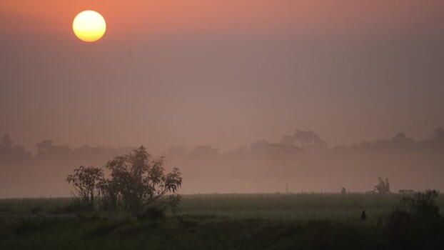 View of a misty sunset over rural fields with a cyclist Bangladesh. View of a misty sunset over rural fields with a cyclist Bangladesh.