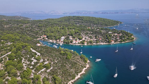 Aerial view of sailboats anchored in the turquoise waters of Necujam bay surrounded by lush green pine forests and coastal houses in Necujam Split Dalmatia County Croatia. Aerial view of sailboats anchored in the turquoise waters of Necujam bay surrounded by lush green pine forests and coastal houses in Necujam Split Dalmatia County Croatia.