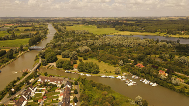 Aerial view of the canal and marina in Saint Omer with docked boats lush green fields and surrounding trees in the countryside of Saint Omer Hauts de France France. Aerial view of the canal and marina in Saint Omer with docked boats lush green fields and surrounding trees in the countryside of Saint Omer Hauts de France France.