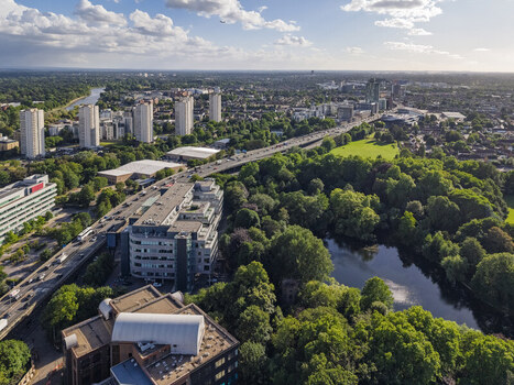 Aerial view of the urban landscape of Brentford featuring high rise residential towers a busy highway and a lush green park with a pond in Brentford England United Kingdom. Aerial view of the urban landscape of Brentford featuring high rise residential towers a busy highway and a lush green park with a pond in Brentford England United Kingdom.