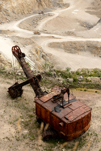 View of an abandoned rusted mechanical shovel in a quarry in the Apuseni Mountains with winding dirt roads and heavy machinery in the background Horea Alba County Romania. View of an abandoned rusted mechanical shovel in a quarry in the Apuseni Mountains with winding dirt roads and heavy machinery in the background Horea Alba County Romania.