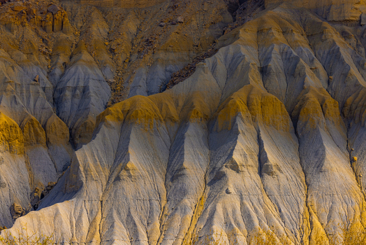 Aerial view of the badlands featuring dramatic geological formations with contrasting yellow and grey sedimentary layers under soft light in Hanksville Utah United States.