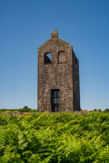 View of a historic stone engine house surrounded by lush green ferns under a clear blue sky in Minions Cornwall United Kingdom. View of a historic stone engine house surrounded by lush green ferns under a clear blue sky in Minions Cornwall United Kingdom.