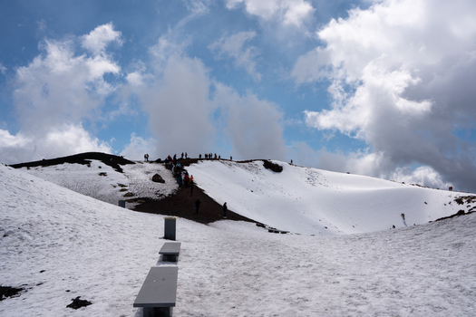 View of a snowy landscape with a path leading to people gathered on a peak under a sky dotted with clouds Taormina Sicily Italy. View of a snowy landscape with a path leading to people gathered on a peak under a sky dotted with clouds Taormina Sicily Italy.
