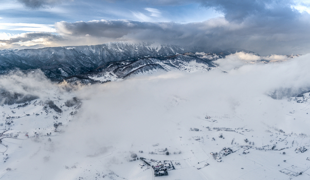 Brasov Romania 21 September 2026 Aerial view of the snow covered Carpathian Mountains landscape with low hanging clouds and small village houses nestled in the valley. Brasov Romania 21 September 2026 Aerial view of the snow covered Carpathian Mountains landscape with low hanging clouds and small village houses nestled in the valley.