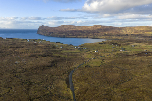 Aerial view of the coastal village with scattered white houses winding roads and rugged moorland overlooking the blue sea Milovaig Scotland United Kingdom.