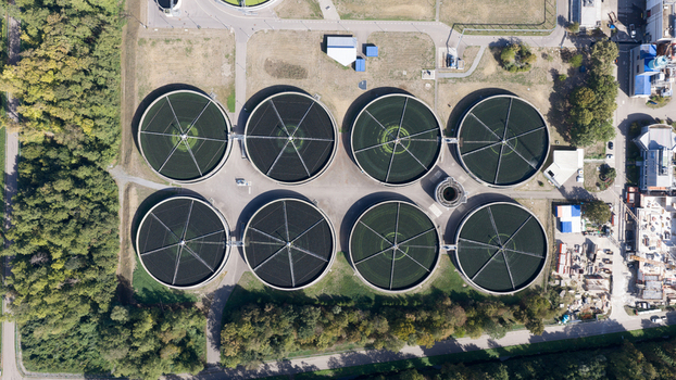 Aerial view of Klarwerk Karlsruhe wastewater treatment plant featuring large circular sedimentation tanks surrounded by trees and industrial infrastructure in Karlsruhe Baden Wurttemberg Germany.