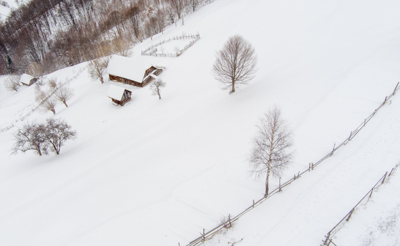 Brasov Romania 21 September 2026 Aerial view of a traditional wooden house surrounded by a snow covered field bare trees and a wooden fence in the winter landscape. Brasov Romania 21 September 2026 Aerial view of a traditional wooden house surrounded by a snow covered field bare trees and a wooden fence in the winter landscape.