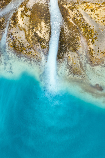 Aerial view of the glacial river in Faueldalen flowing into the turquoise waters of the fjord with rocky banks and sediment rich water in Jovik Troms Norway.