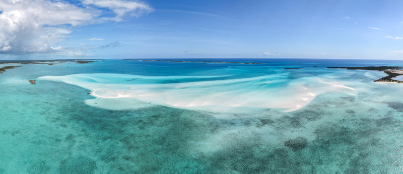 Aerial view of the Man O War Cay Sandbar stretching through turquoise tropical waters under a clear blue sky with small boats anchored nearby in Rolletown Exuma The Bahamas. Aerial view of the Man O War Cay Sandbar stretching through turquoise tropical waters under a clear blue sky with small boats anchored nearby in Rolletown Exuma The Bahamas.