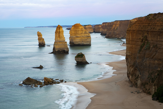 View of the Twelve Apostles limestone stacks standing in the calm ocean along the sandy beach and steep cliffs Australia. View of the Twelve Apostles limestone stacks standing in the calm ocean along the sandy beach and steep cliffs Australia.