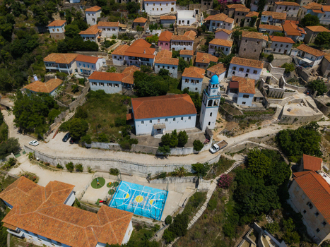 Aerial view of the historic village featuring white houses with red roofs a church with a blue dome and a blue basketball court in Dhermi Vlore County Albania. Aerial view of the historic village featuring white houses with red roofs a church with a blue dome and a blue basketball court in Dhermi Vlore County Albania.