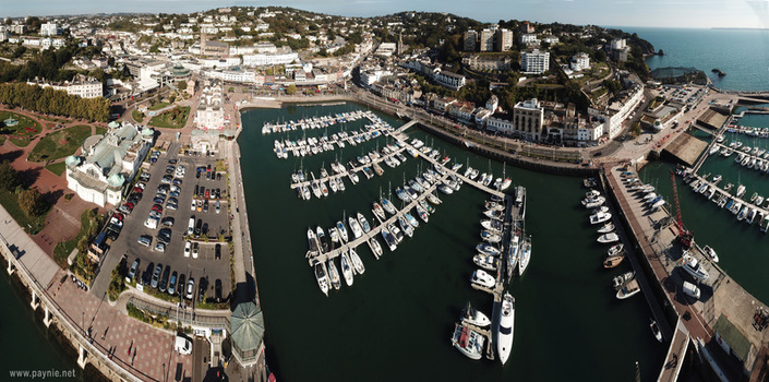 Aerial view of the bustling marina filled with white yachts and sailboats moored at docks alongside the coastal town architecture Torquay England United Kingdom.