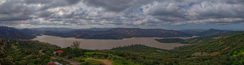 Aerial view of the landscape reveals a tranquil reservoir reflecting the overcast sky surrounded by rolling hills and lush greenery Castellar de la Frontera Andalusia Spain. Aerial view of the landscape reveals a tranquil reservoir reflecting the overcast sky surrounded by rolling hills and lush greenery Castellar de la Frontera Andalusia Spain.