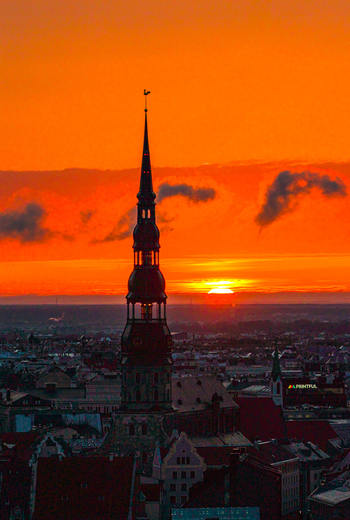 Aerial view of St. Peter s Church spire silhouetted against a vibrant orange sunset over the historic rooftops of Riga Latvia. Aerial view of St. Peter s Church spire silhouetted against a vibrant orange sunset over the historic rooftops of Riga Latvia.