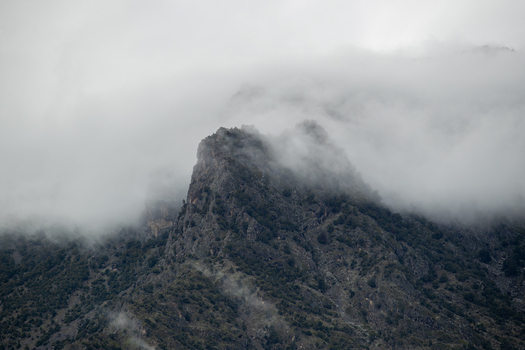 View of a rugged mountain peak partially covered by dense clouds and mist with rocky slopes and sparse vegetation Chilas Gilgit Pakistan. View of a rugged mountain peak partially covered by dense clouds and mist with rocky slopes and sparse vegetation Chilas Gilgit Pakistan.