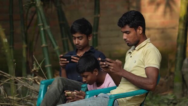 View of three young men using smartphones outdoors Bangladesh. View of three young men using smartphones outdoors Bangladesh.
