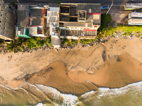 Aerial view of beachfront buildings and people on the sandy shore with waves crashing against the coast in Galle Southern Province Sri Lanka.