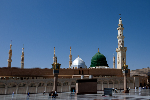 View of Al Masjid e Nabawi with its iconic green dome silver dome and minarets under a clear blue sky in the courtyard of the mosque in Madinah Al Madinah Province Saudi Arabia. View of Al Masjid e Nabawi with its iconic green dome silver dome and minarets under a clear blue sky in the courtyard of the mosque in Madinah Al Madinah Province Saudi Arabia.