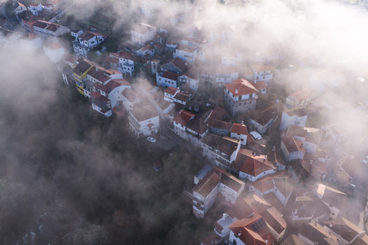 Aerial view of the historic village of Avo shrouded in thick morning fog with red tiled roofs peeking through the mist in Oliveira do Hospital Coimbra District Portugal.
