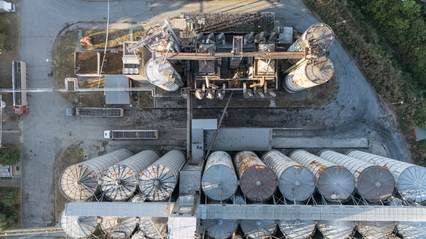 Aerial view of a large industrial grain silo facility with multiple cylindrical storage tanks pipes and trucks parked on the surrounding paved grounds in Sremska Mitrovica Vojvodina Serbia. Aerial view of a large industrial grain silo facility with multiple cylindrical storage tanks pipes and trucks parked on the surrounding paved grounds in Sremska Mitrovica Vojvodina Serbia.
