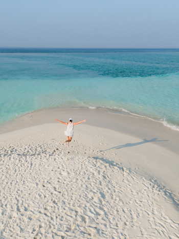 Aerial view of a woman standing on a pristine white sandbar with arms outstretched embraced by turquoise waters Dhidhdhoo Thiladhunmathi Atoll Maldives.