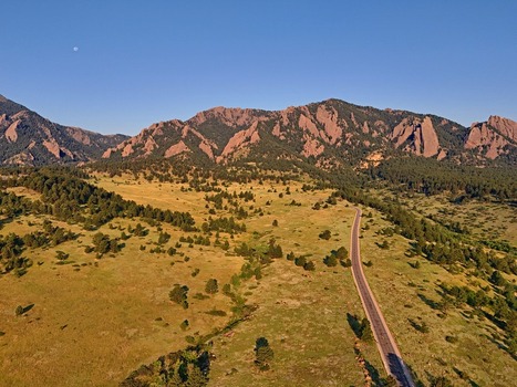 Aerial view of the NCAR UCAR Foothills Laboratory nestled against the rugged Flatirons with a winding road cutting through grassy foothills in Boulder Colorado United States.