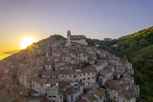 Aerial view of the historic hilltop town of Artena with stone buildings terracotta rooftops and a church tower illuminated by the warm sunset light in Artena Lazio Italy.