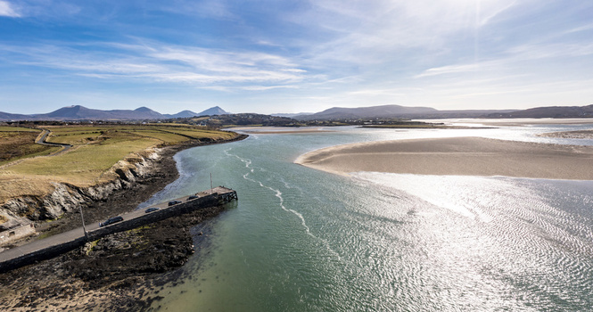 Aerial view of Ballyness Bay featuring a stone pier extending into turquoise water surrounded by rugged coastline green fields and distant mountains in Ballyness County Donegal Ireland. Aerial view of Ballyness Bay featuring a stone pier extending into turquoise water surrounded by rugged coastline green fields and distant mountains in Ballyness County Donegal Ireland.