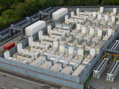 Aerial view of a data center with rows of cooling units and server infrastructure enclosed by a metal fence in the United Kingdom.
